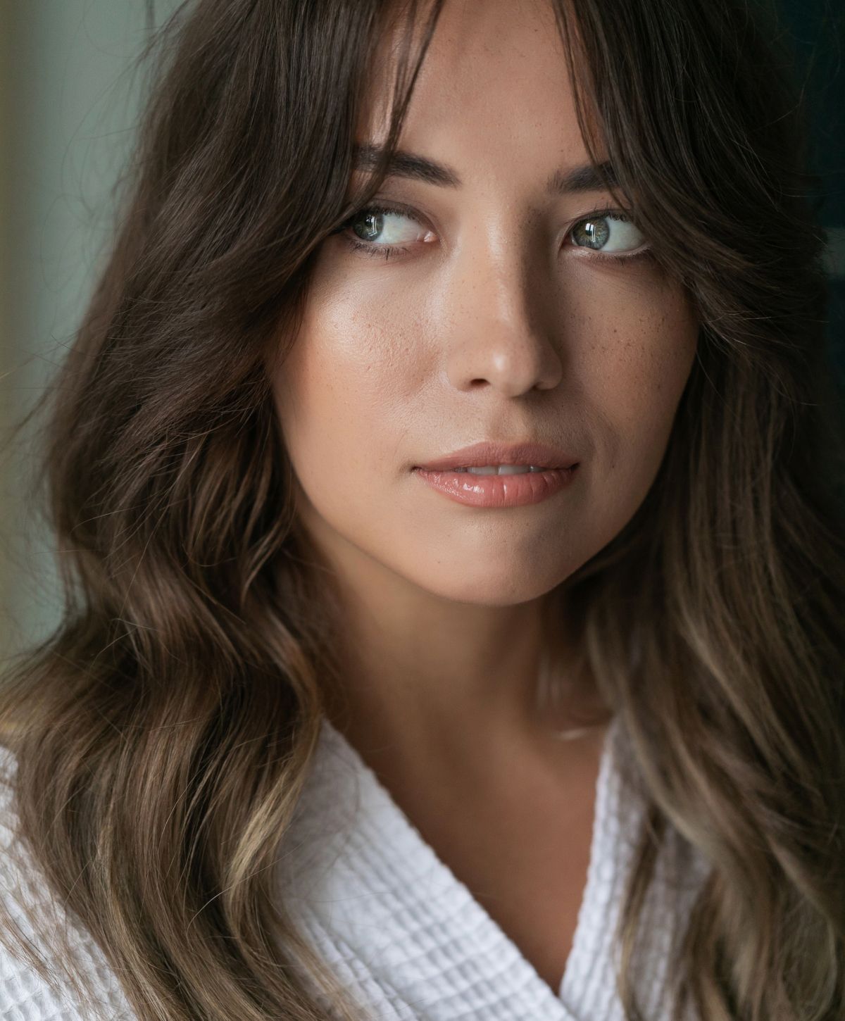 Woman with wavy hair in a robe, thoughtful expression.
