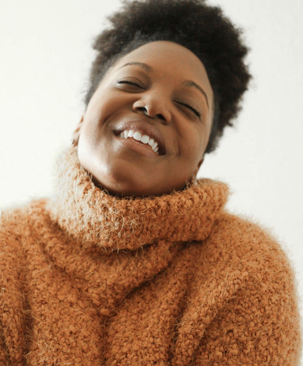 Smiling person wearing an orange turtleneck sweater.